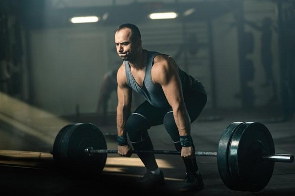muscular build man making an effort while weightlifting during cross training in a gym