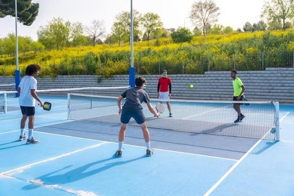 four multiethnic friends playing pickleball in an outdoor court