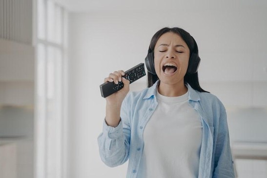 female singing karaoke using tv remote control like a mic listening to music in headphones at home